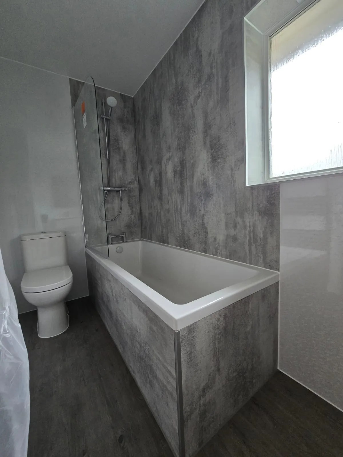 Modern bathroom with a white bathtub, gray textured wall panels, and a white toilet beside it.
