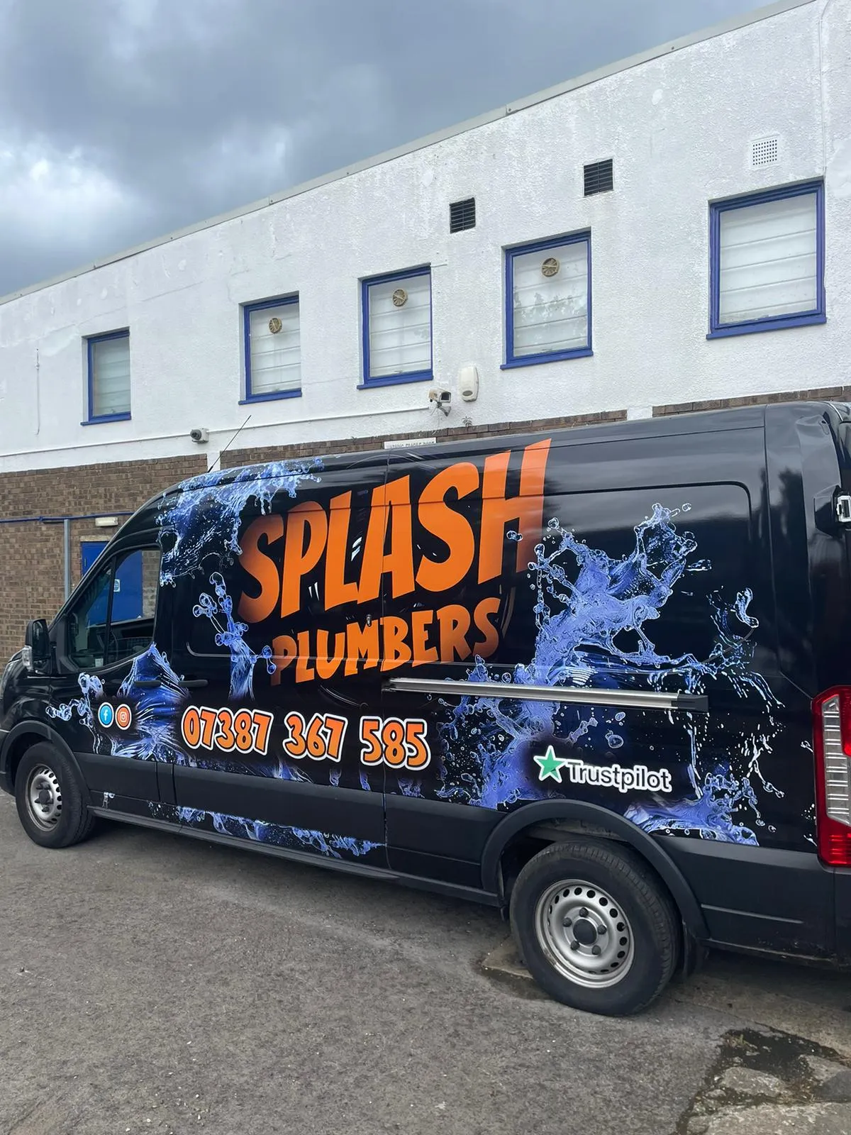 Black van with Splash Plumbers branding, water splash graphics, phone number, and Trustpilot logo.