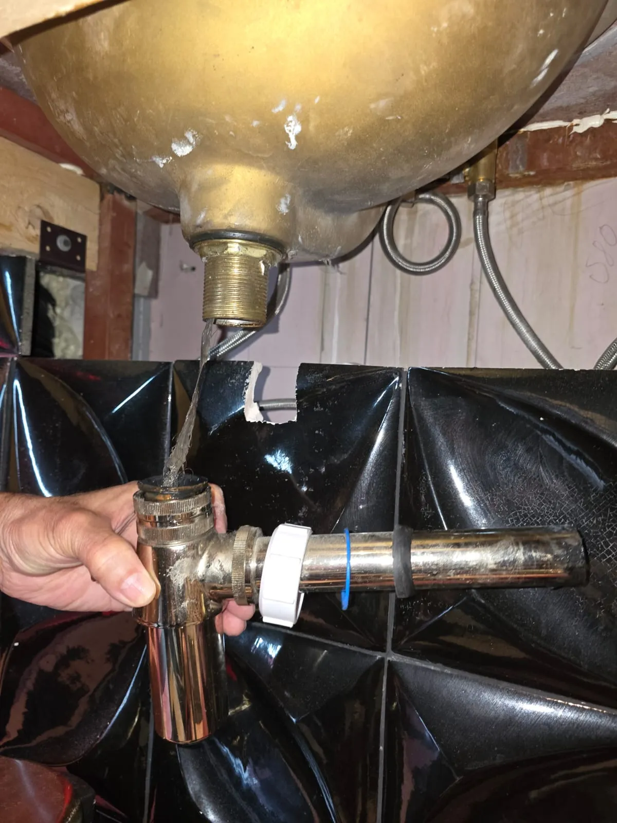 Hand holding a chrome plumbing trap fitting under a sink drain with water flowing into it.