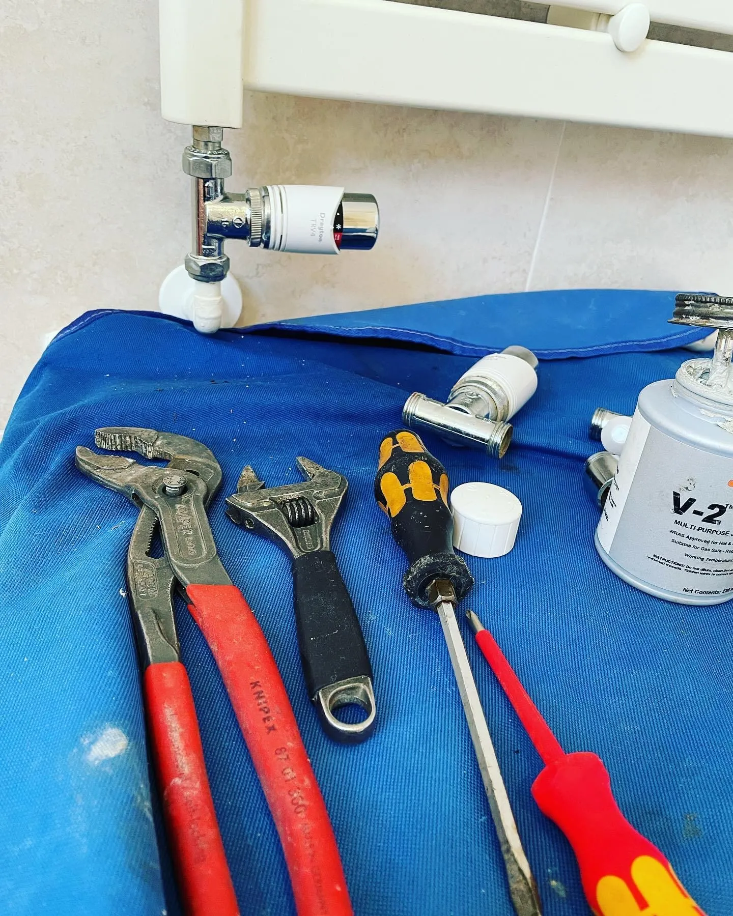 Plumbing tools including pliers, wrench, and screwdrivers laid on a blue cloth under a radiator valve.